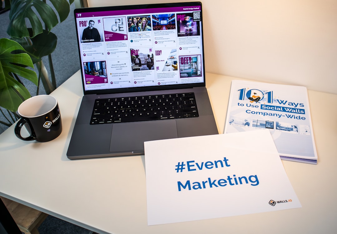 A desk with documents, a piece of paper with the hashtag #EventMarketing and a laptop showing a social media wall